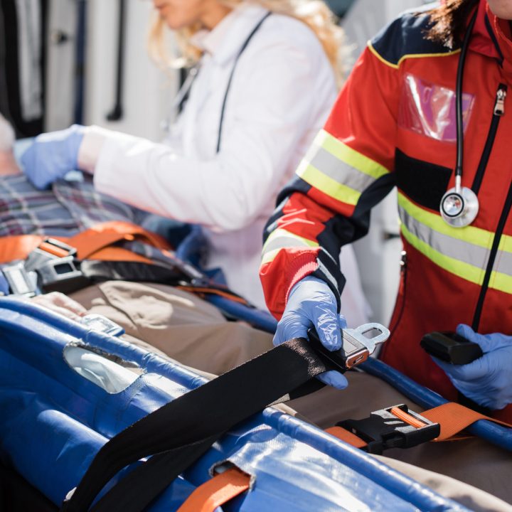 Selective focus of paramedic holding belts of stretcher near patient and colleagues outdoors Selective focus of paramedic holding belts of stretcher near patient and colleagues outdoors